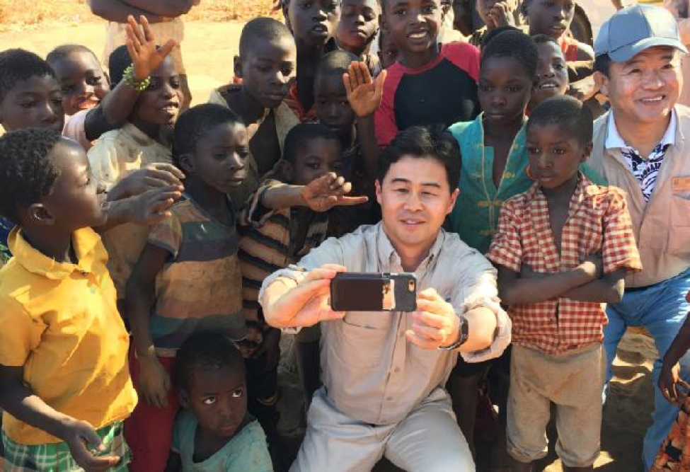 Nu Skin employee takes a selfie with a large group of Malawi children behind him posing for a picture.
